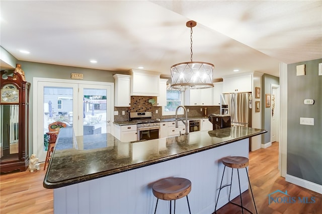 kitchen featuring appliances with stainless steel finishes, white cabinets, light hardwood / wood-style floors, and pendant lighting