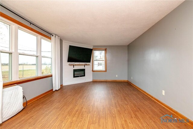 unfurnished living room with light hardwood / wood-style floors, a textured ceiling, and a healthy amount of sunlight