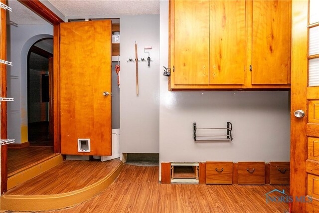 washroom with a textured ceiling, light hardwood / wood-style flooring, and cabinets