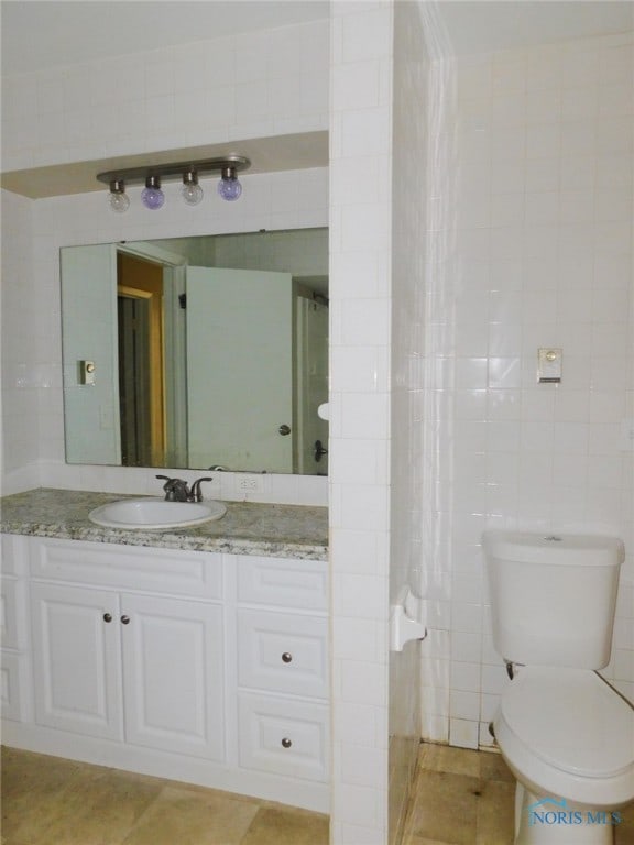 bathroom with tile walls, vanity, toilet, and tile patterned flooring