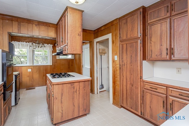 kitchen featuring a center island, hanging light fixtures, white gas cooktop, and wood walls