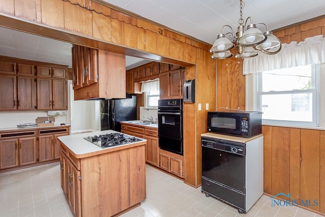 kitchen with a kitchen island, sink, black appliances, a notable chandelier, and wood walls