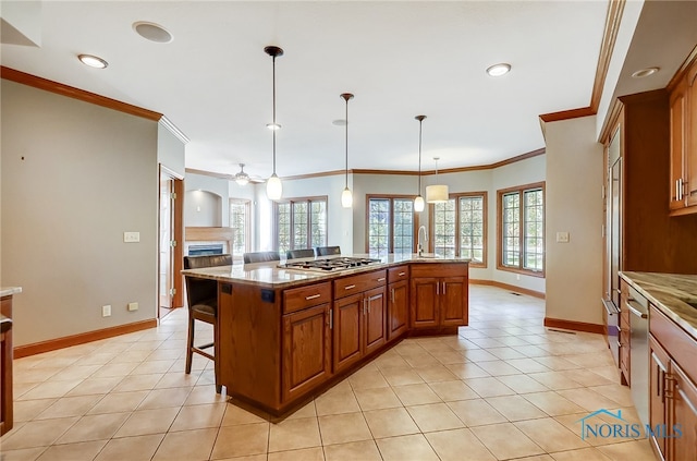 kitchen featuring a kitchen island with sink, ornamental molding, pendant lighting, stainless steel gas stovetop, and ceiling fan