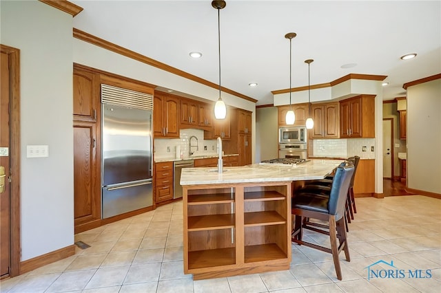 kitchen with pendant lighting, built in appliances, a kitchen island with sink, and tasteful backsplash