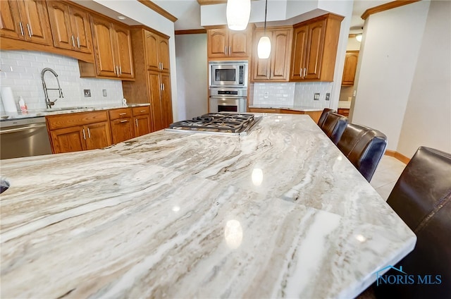 kitchen with tasteful backsplash, light stone countertops, sink, pendant lighting, and stainless steel appliances