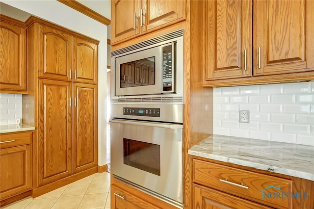 kitchen featuring tasteful backsplash, light stone countertops, appliances with stainless steel finishes, light tile patterned flooring, and crown molding