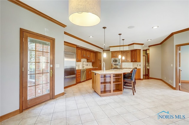 kitchen with a center island with sink, ornamental molding, built in appliances, pendant lighting, and sink