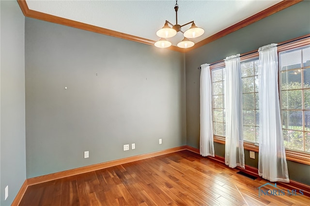 spare room with hardwood / wood-style floors, crown molding, and an inviting chandelier