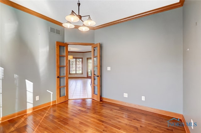 unfurnished room with crown molding, hardwood / wood-style flooring, a chandelier, and french doors