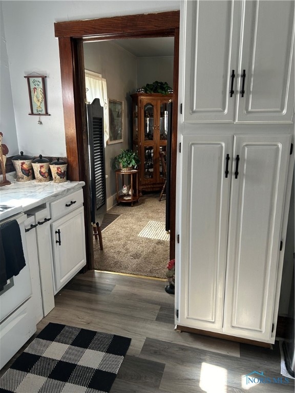 interior space with white range, dark colored carpet, and white cabinets