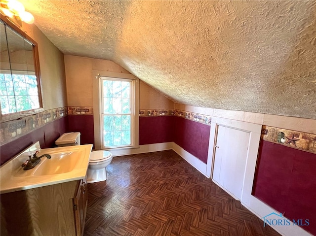 bathroom with toilet, parquet flooring, vaulted ceiling, vanity, and a textured ceiling