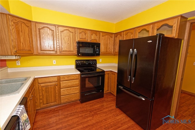 kitchen with a textured ceiling, hardwood / wood-style flooring, black appliances, and sink