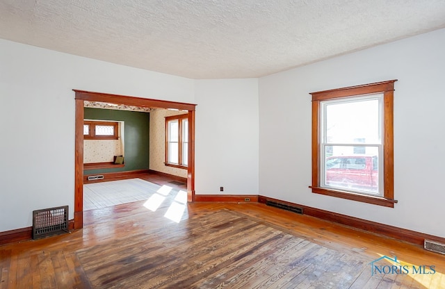 unfurnished room with a textured ceiling, wood-type flooring, and a wealth of natural light