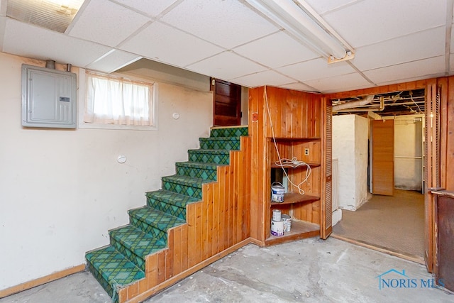 basement with electric panel, a paneled ceiling, and wood walls