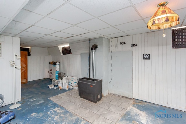 basement with a drop ceiling and wooden walls