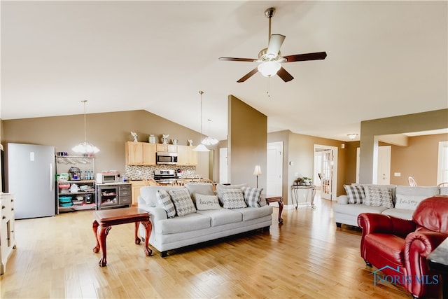 living room featuring ceiling fan with notable chandelier, light wood-type flooring, and vaulted ceiling