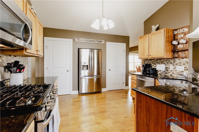 kitchen with hanging light fixtures, backsplash, light hardwood / wood-style flooring, sink, and stainless steel appliances