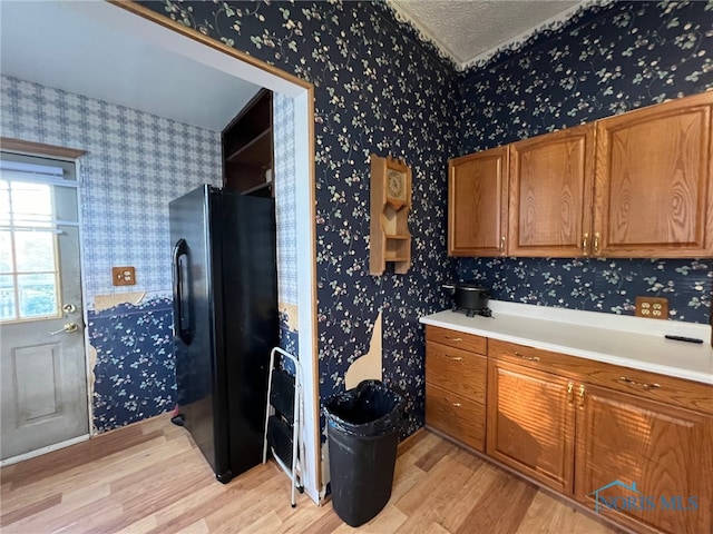 kitchen with black refrigerator, light wood-type flooring, and a textured ceiling