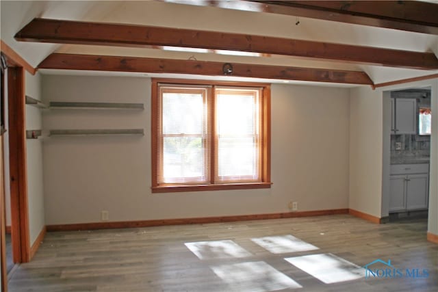 unfurnished bedroom featuring beam ceiling, ensuite bathroom, and light wood-type flooring