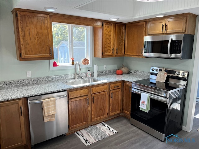 kitchen with light stone counters, appliances with stainless steel finishes, sink, and hardwood / wood-style floors