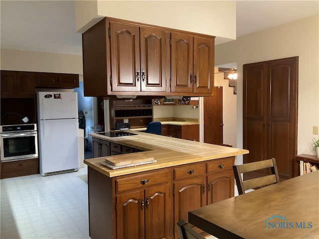 kitchen featuring black electric stovetop, stainless steel oven, and white fridge