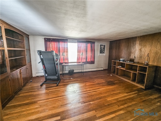 unfurnished room featuring baseboard heating, wooden walls, and dark hardwood / wood-style flooring