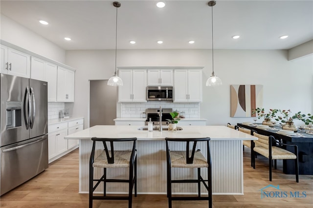 kitchen featuring light hardwood / wood-style flooring, white cabinets, decorative light fixtures, and stainless steel appliances