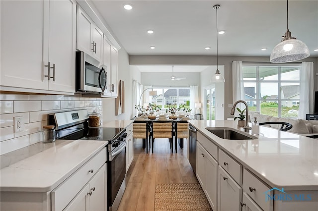 kitchen featuring hanging light fixtures, stainless steel appliances, sink, white cabinets, and light hardwood / wood-style floors