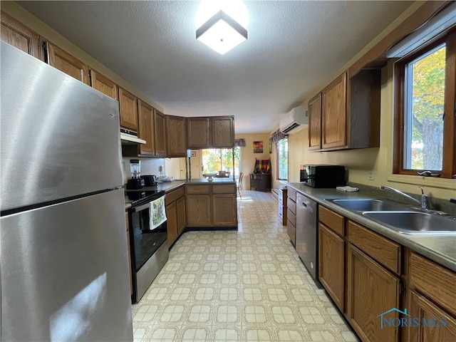 kitchen featuring an AC wall unit, stainless steel appliances, a textured ceiling, and sink