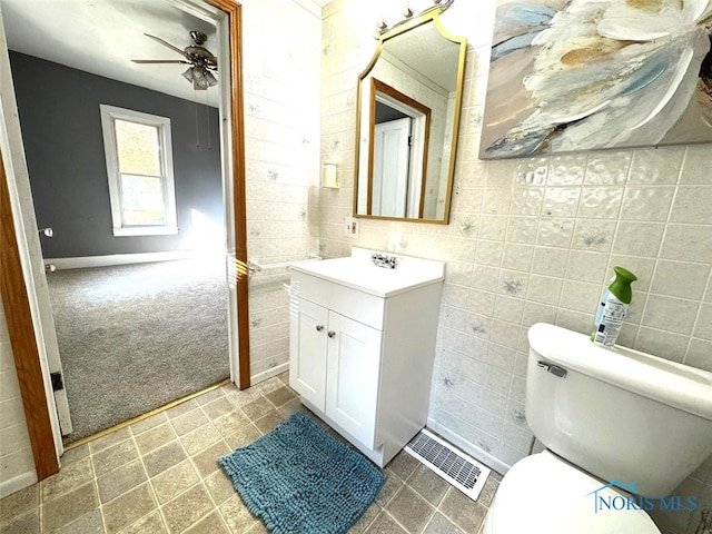 bathroom featuring toilet, vanity, tile walls, and ceiling fan