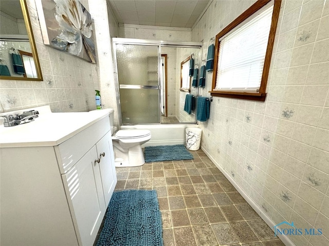 full bathroom featuring tile walls, vanity, enclosed tub / shower combo, and toilet