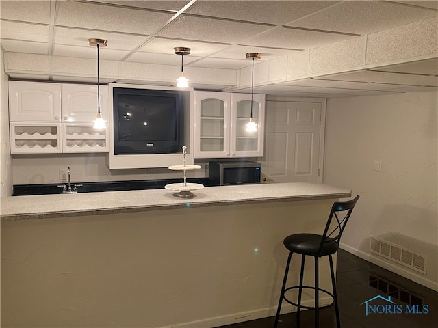 bar featuring a paneled ceiling, white cabinets, and dark tile patterned flooring