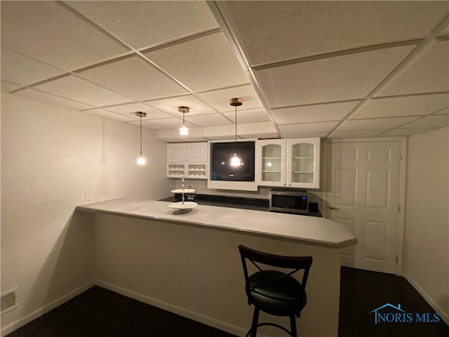 bar featuring a drop ceiling, white cabinetry, and pendant lighting