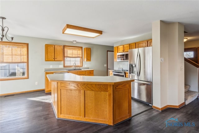 kitchen with appliances with stainless steel finishes, dark hardwood / wood-style flooring, a kitchen island, and hanging light fixtures