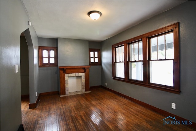 unfurnished living room featuring a tile fireplace, plenty of natural light, and dark hardwood / wood-style flooring