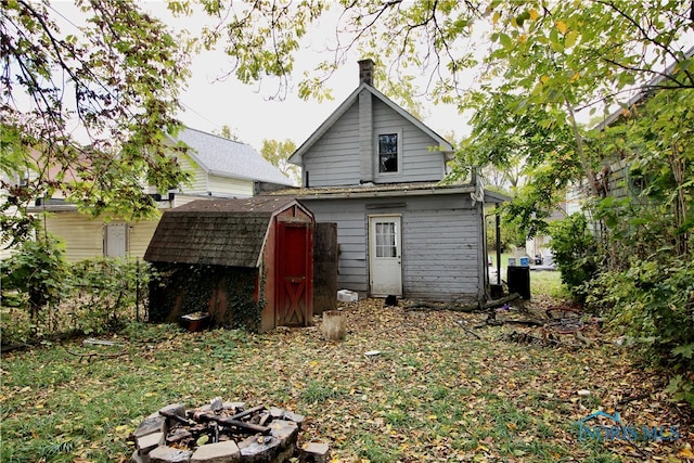 back of house featuring an outdoor fire pit and a storage unit