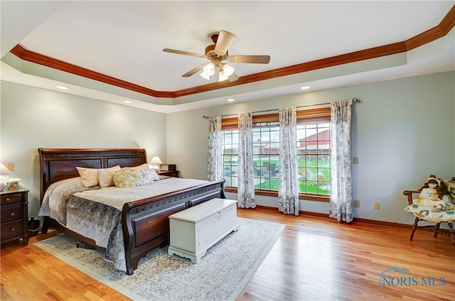 bedroom with a tray ceiling, ceiling fan, crown molding, and light hardwood / wood-style floors