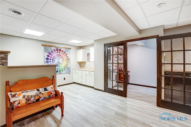 living area with light hardwood / wood-style flooring, a drop ceiling, and french doors