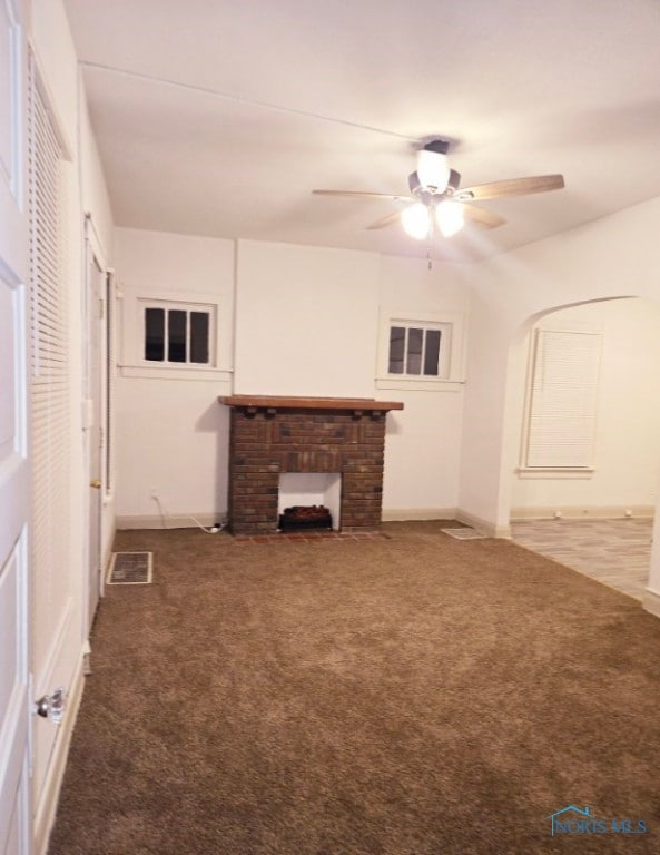 unfurnished living room with a brick fireplace, carpet floors, and ceiling fan