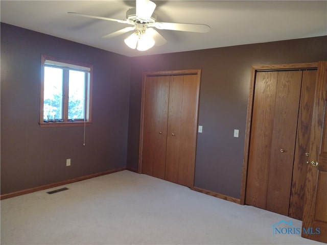 unfurnished bedroom with ceiling fan, multiple closets, and light colored carpet