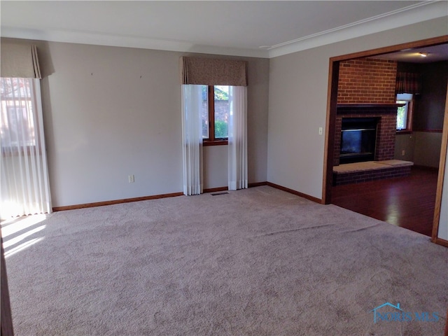 unfurnished living room featuring crown molding, a brick fireplace, and carpet floors