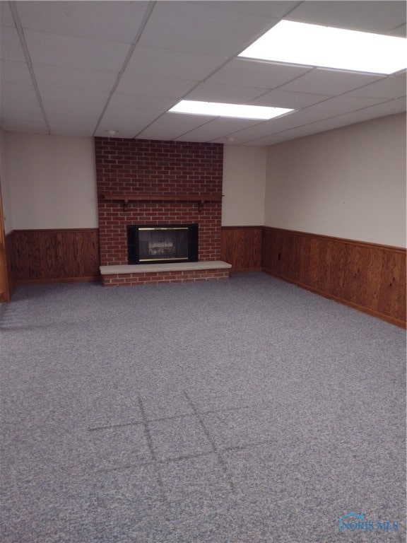 basement with a paneled ceiling, wooden walls, carpet flooring, and a brick fireplace