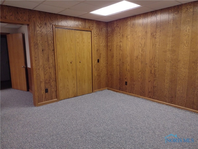 empty room with a paneled ceiling, wood walls, and carpet