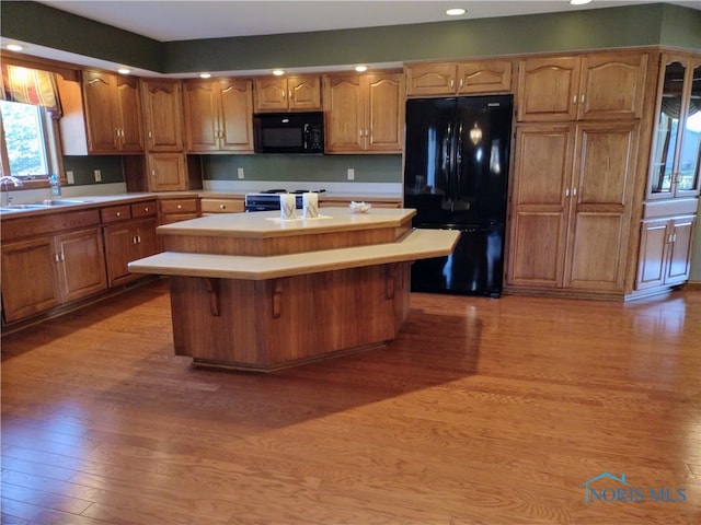 kitchen with black appliances, light hardwood / wood-style flooring, a kitchen bar, and a kitchen island