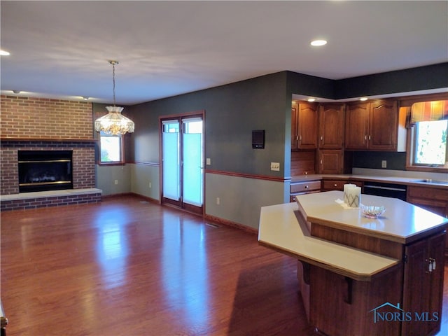 kitchen featuring dishwasher, dark wood-type flooring, a center island, decorative light fixtures, and a fireplace