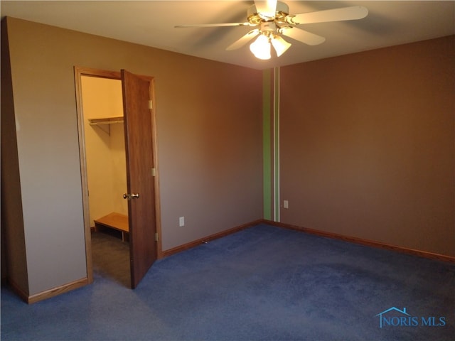 unfurnished bedroom with dark carpet, a spacious closet, a closet, and ceiling fan