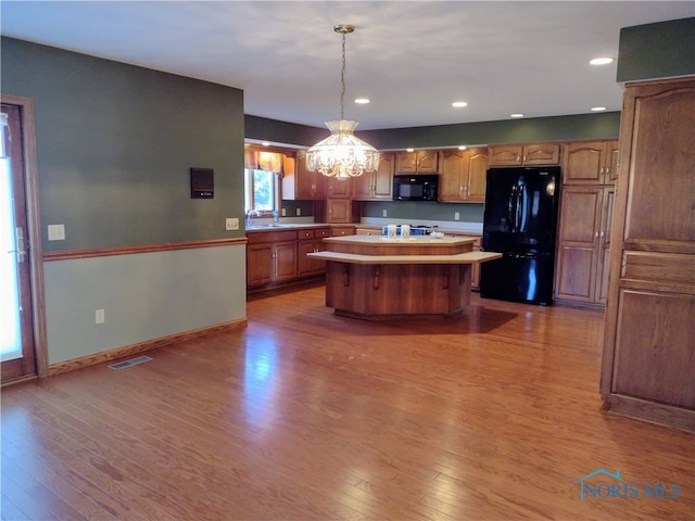 kitchen featuring hardwood / wood-style floors, black appliances, hanging light fixtures, and a kitchen island