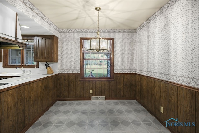 unfurnished dining area featuring sink, an inviting chandelier, and wood walls