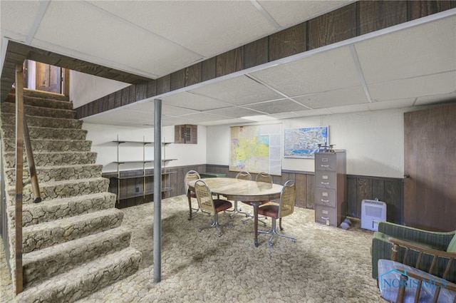 basement featuring wooden walls, a paneled ceiling, and carpet floors