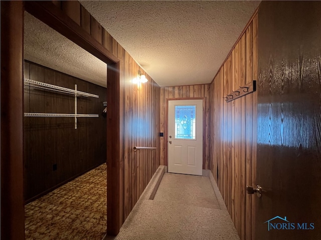 doorway with wood walls, carpet floors, and a textured ceiling